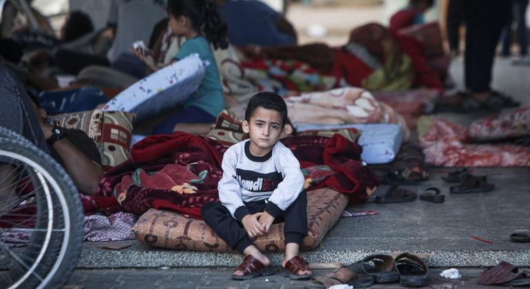 Un garçon de cinq ans est assis sur son matelas dans la cour d'un abri, entouré de plusieurs centaines d'autres personnes déplacées.