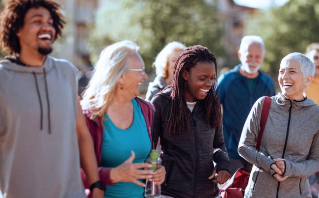 A group of people wearing workout clothes laugh together while standing outside.