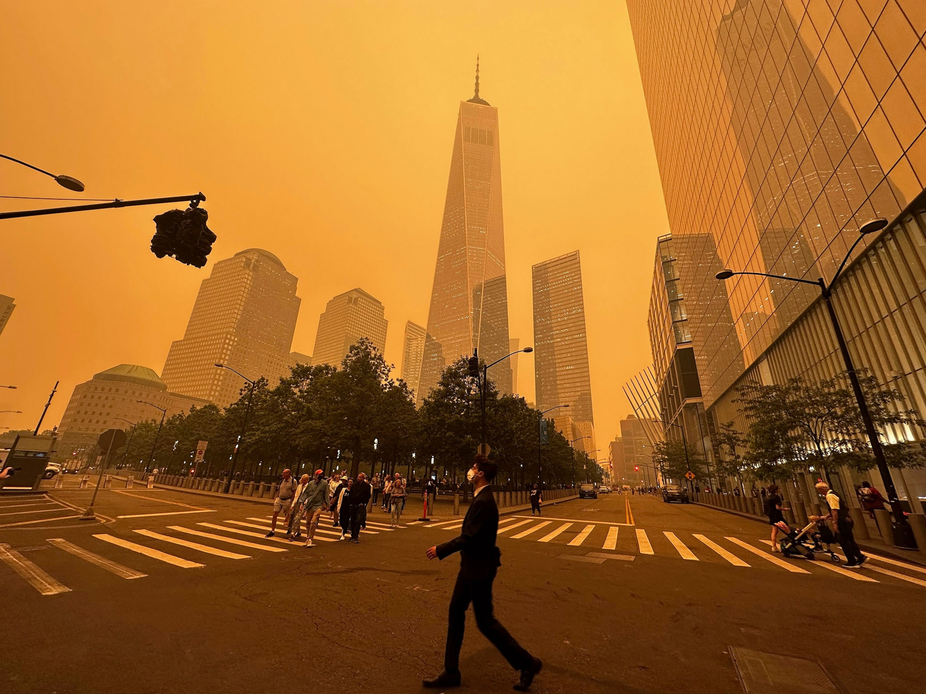 A Man crosses an intersection deep orange haze colors the city.