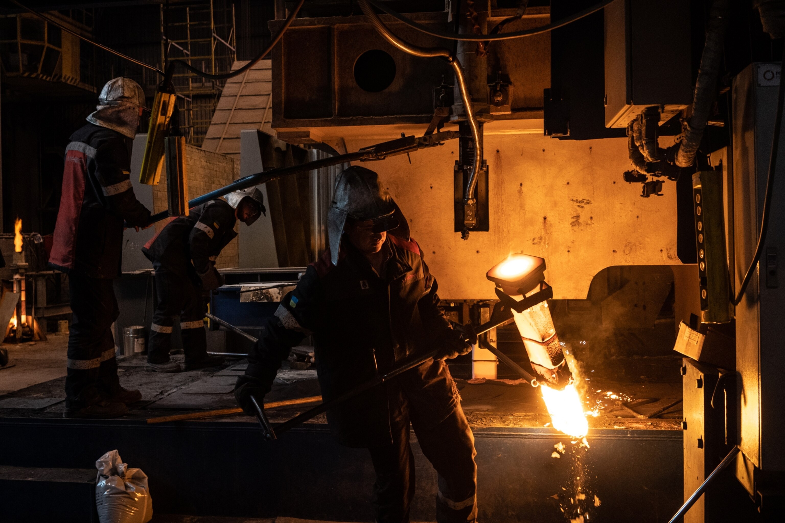 workers in heavy suits work with molten metals in the Iliych plant