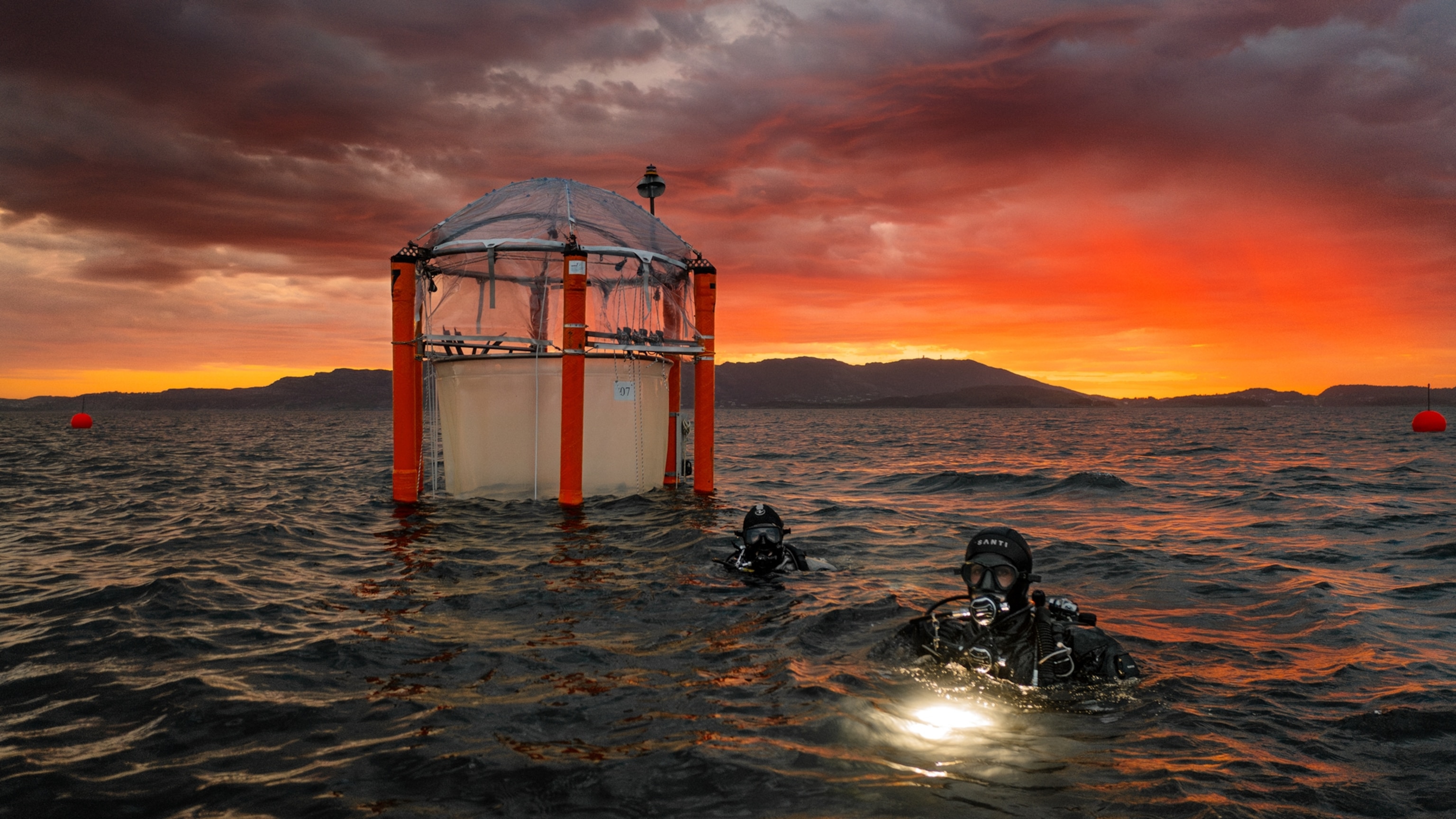 Diver in wetsuit next to free-floating experimental enclosures.