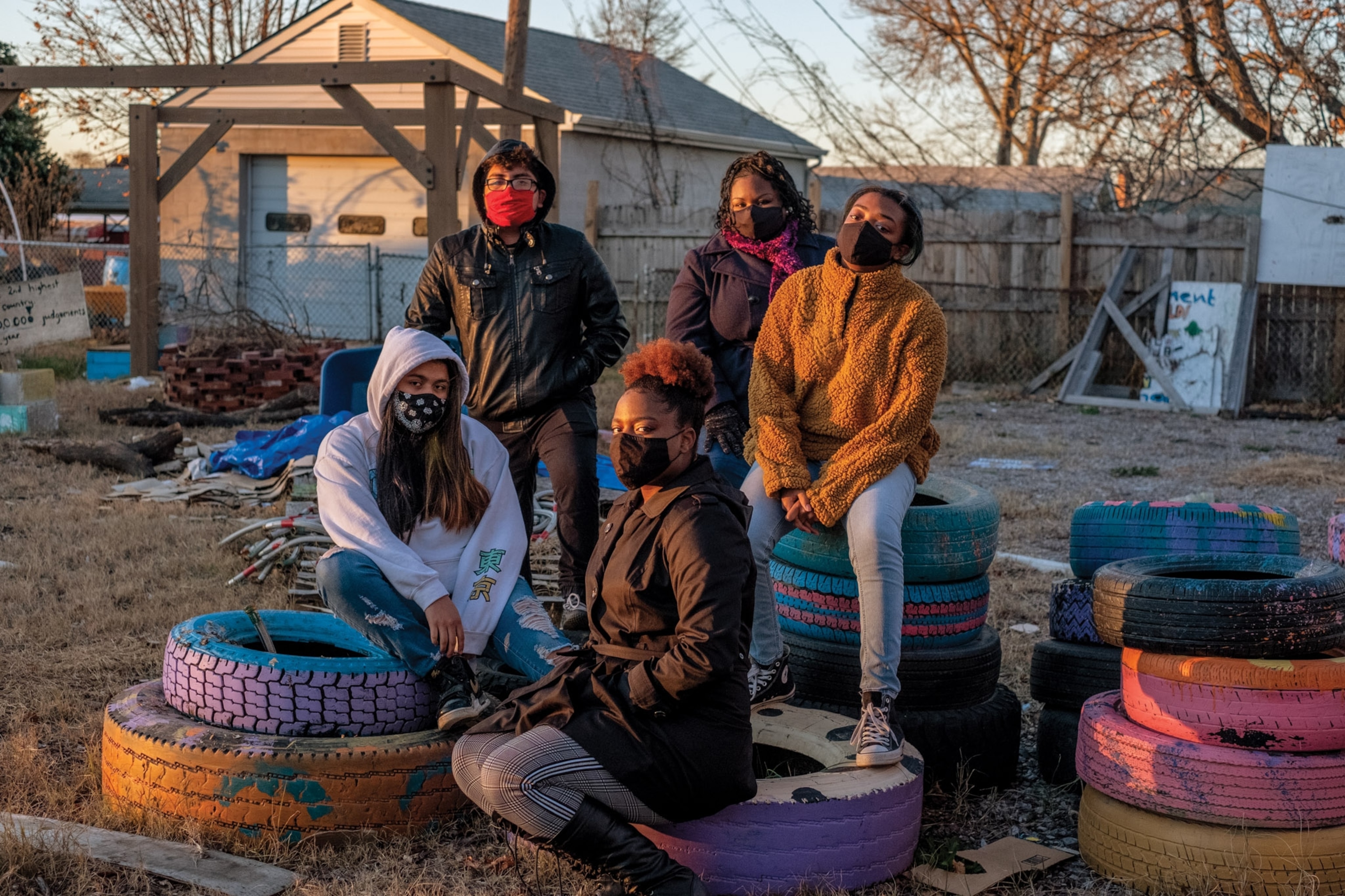 A group of youth sit on tires with natural light and face masks.