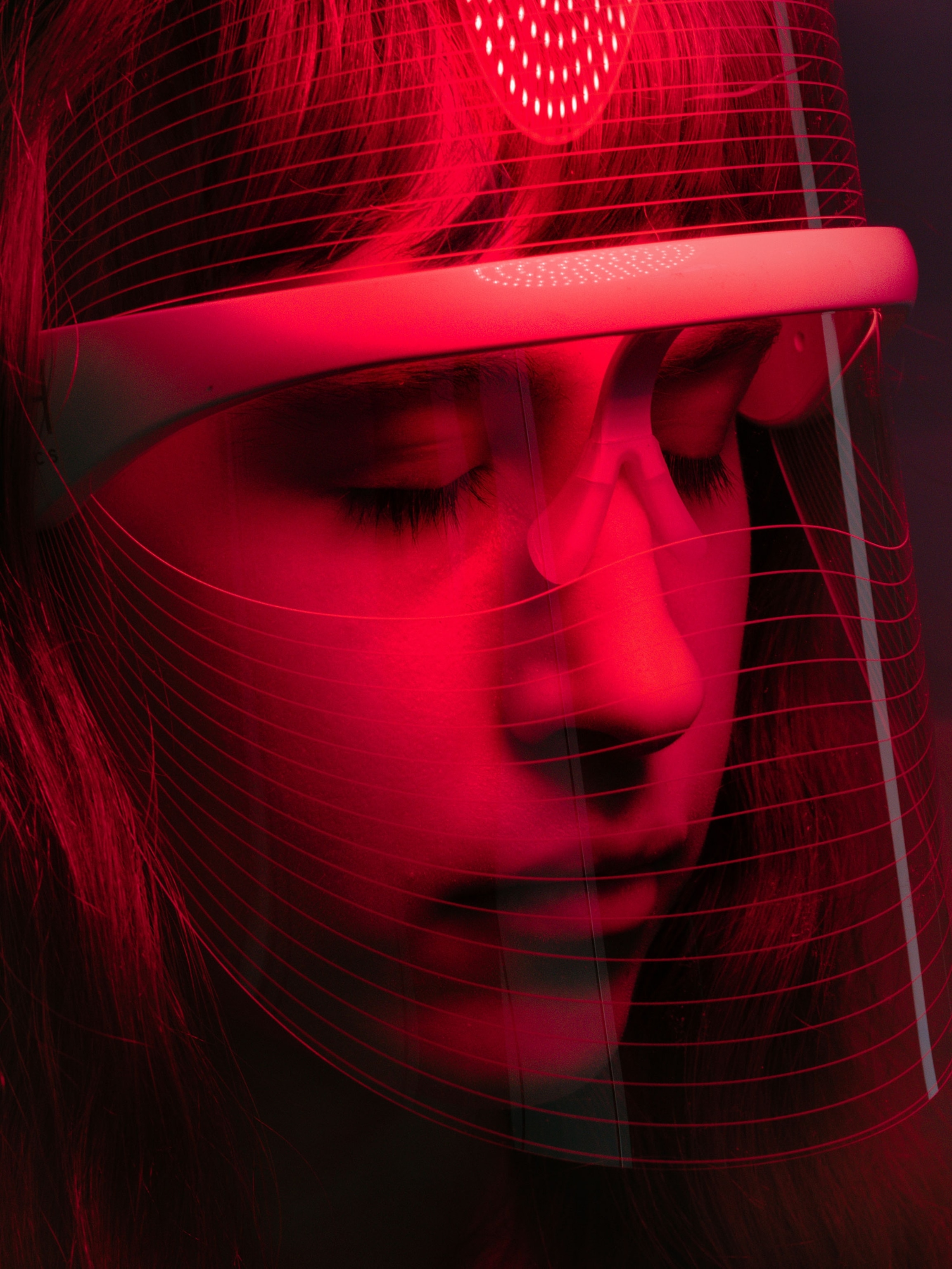 A model poses for a portrait with a LED Light Shield Mask From DM Aesthetics designed for consumer use in a studio against a blue background