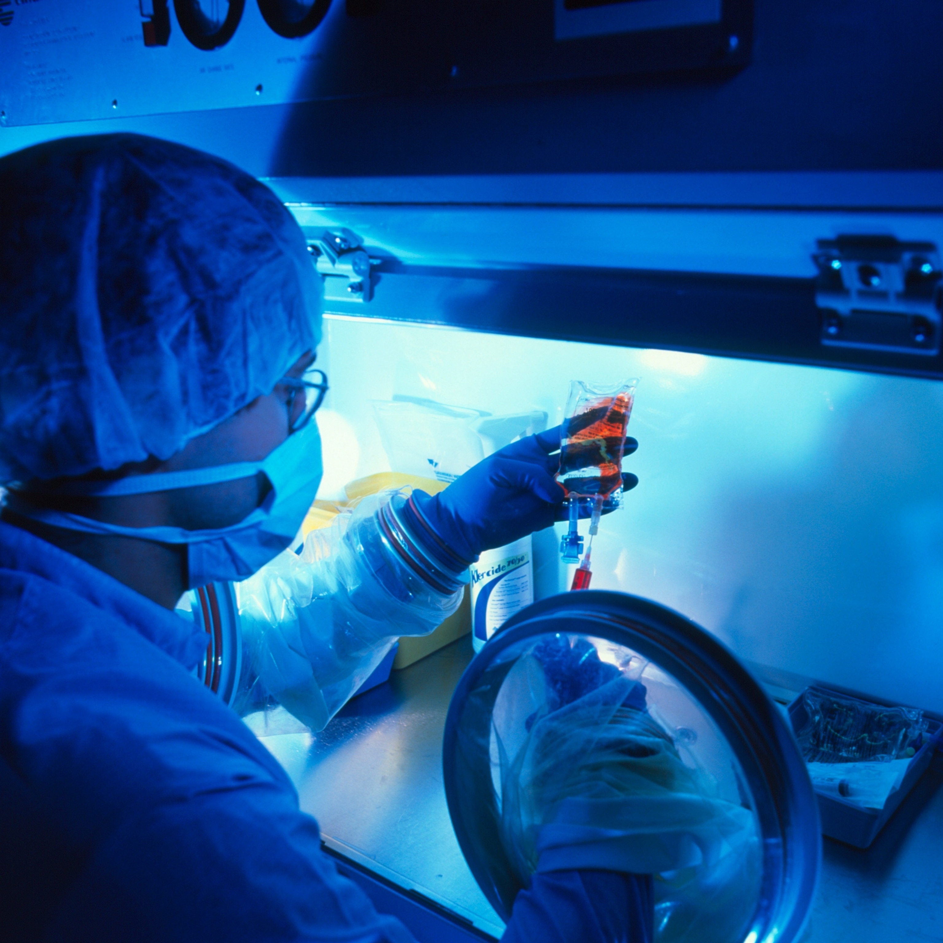 Male pharmacist injecting doxorubicin into an intravenous (IV) drip bag in the cytotoxic unit of a hospital cancer ward.