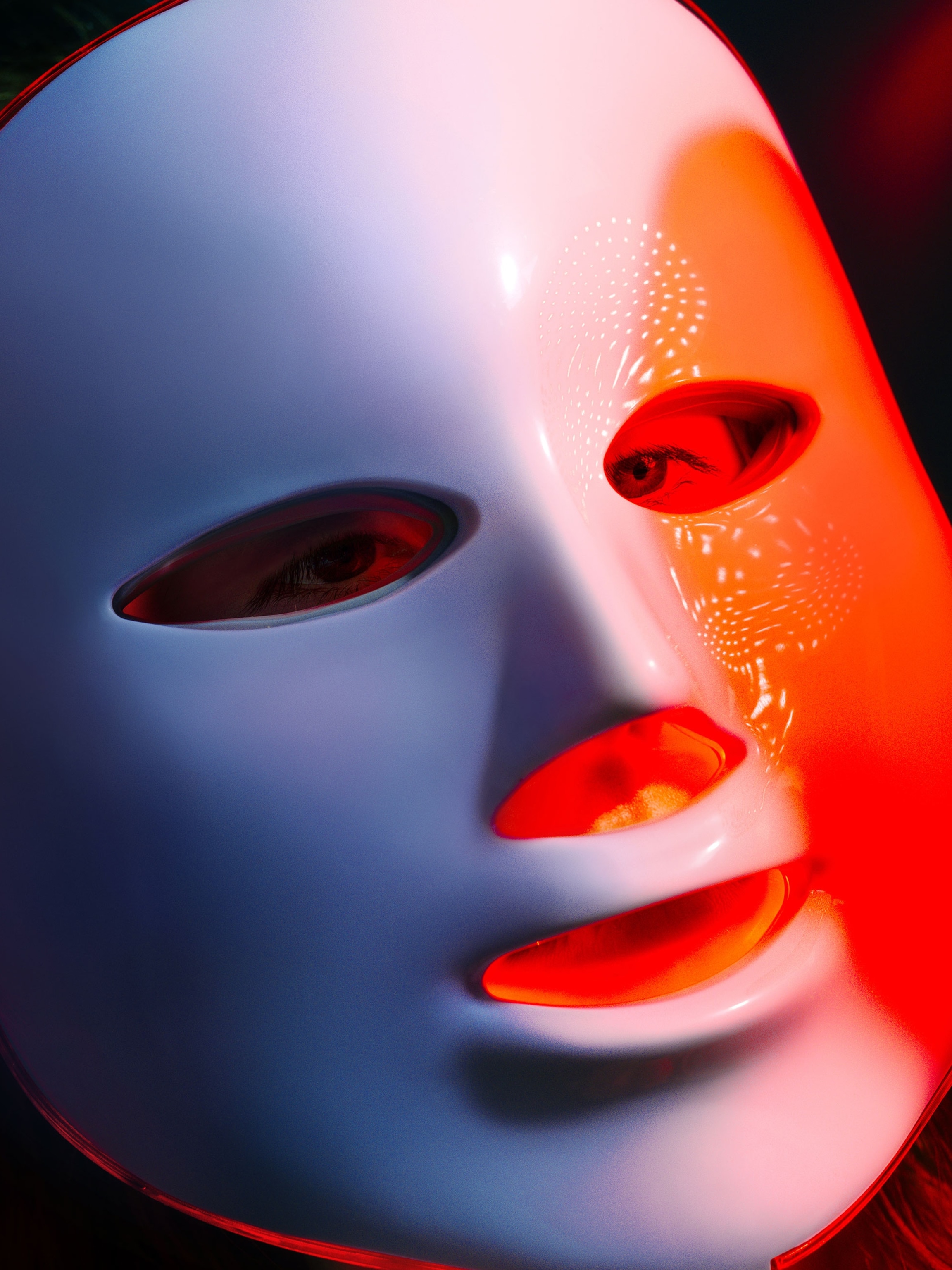 A model poses for a portrait with a red light LED mask designed for consumer use in a studio against a blue background