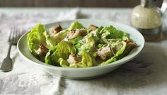 a white bowl filled with lettuce and meat on top of a tablecloth