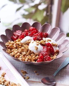 a bowl filled with granola, yogurt and strawberries on top of a table