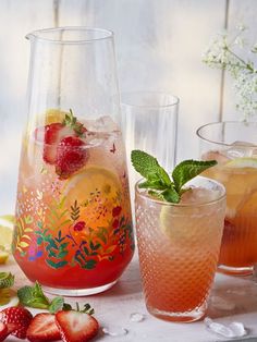 three glasses filled with different types of drinks next to lemons and strawberries on a table