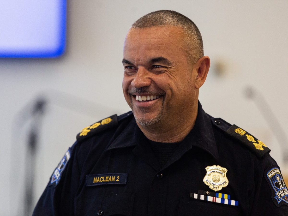 A Black man with short hair and goatee wearing a black police uniform smiles and looks to the left of the frame.