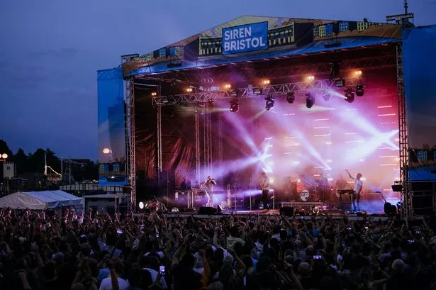 General view of stage with musicians and large crowd outdoors