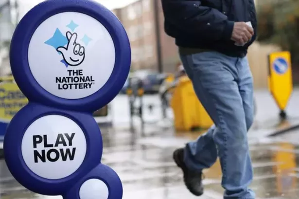 Pictured is a man walking past a National Lottery sign