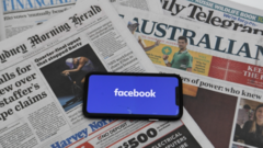 A phone showing the Facebook logo on a spread of Australian newspapers