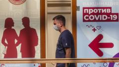 Человек в маске на фоне плаката "Вакцинация против Covid-19"