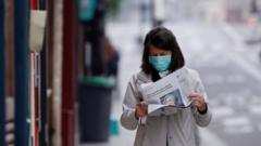 A woman wearing a protective face mask reads a newspaper as she walks in a street on the deserted Ile Saint Louis in Paris