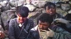 Group of men with chains around their necks sit by a wall on a mountain top