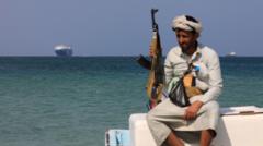 Вооруженный йеменец на фоне захваченного хуситами торгового судна Galaxy Leader 5 декабря 2023 года