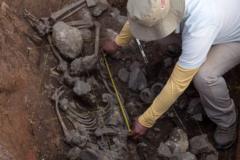Археолог с измерительной лентой около скелета