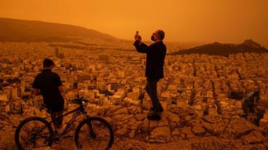 A man takes a photograph of the city of Athens from Tourkovounia hill, as southerly winds carry waves of Saharan dust to the city, in Athens, on April 23, 2024.