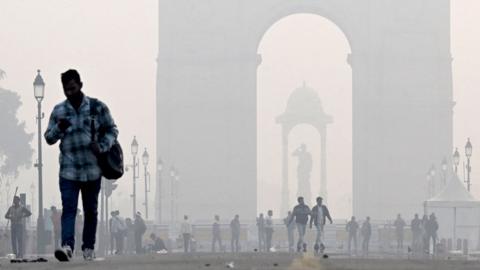 People walk along the Kartavya Path in front of the India Gate amid heavy smoggy conditions in New Delhi on 13 November 2023