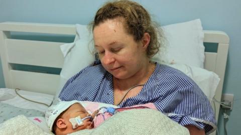 Katie Fowler in a hospital bed holding her daughter Abigail Fowler Miller with tubes attached to her