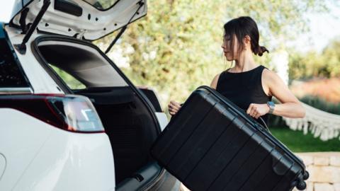 Woman putting luggage in back of a car