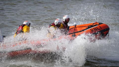 Four crew members on an RNLI lifeboat in the water with water splashing up