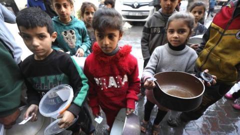Children in Gaza wait with empty pots at a food distribution point