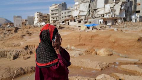A woman stands in front of destroyed houses in Derna, Libya