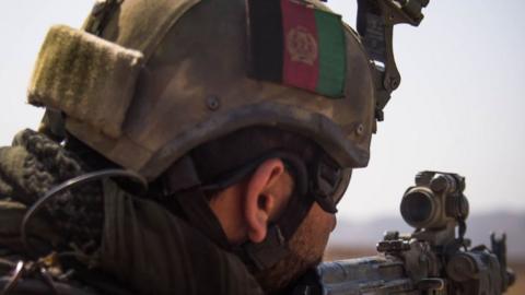 An Afghan soldier seen from behind looking through the sight of a rifle, wearing a combat helmet