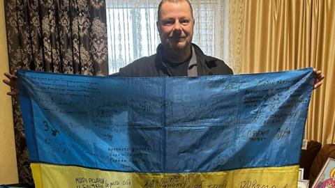 Elliott Svatos holding a Ukrainian flag covered in signatures