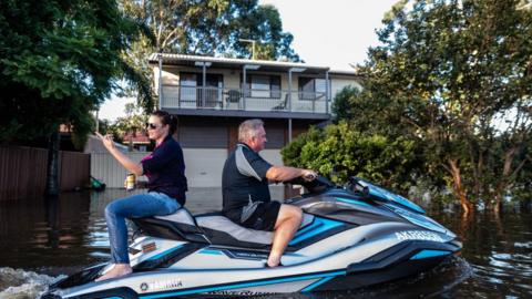 People are seen on a jet-sky in a street affected by the flood on March 23, 2021 in Windsor, NSW