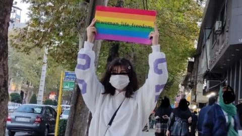 A young Iranian woman holds rainbow flag with the hashtag 'woman, life, freedom'