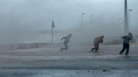 People run through sea spray in Rhyl, north Wales