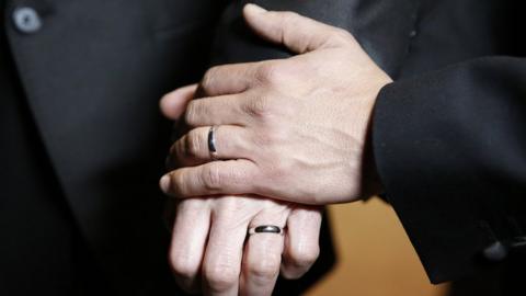 Two men hold hands with wedding rings on after one of the first gay weddings in England in 2014.