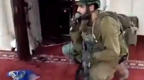 Still frame of Israeli soldier using a microphone to recite a prayer in a mosque in Jenin