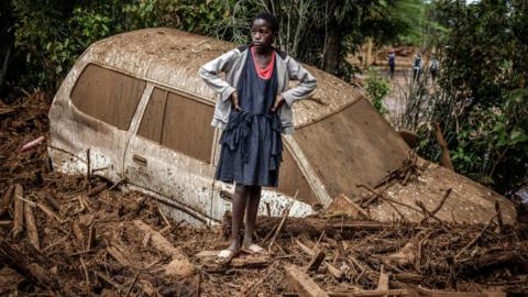 A girl looks on next to a damaged car buried in mud in an area that was heavily affected by torrential rains and flash floods in the village of Kamuchiri, near Mai Mahiu, on April 29, 2024