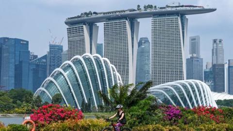 A woman rides her bicycle with the Marina Bay Sands hotel and high rise buildings in the background in Singapore on September 4, 2023.