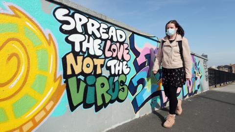 A woman walks past street art that reads "Spread the love not the virus" in Hull, Yorkshire