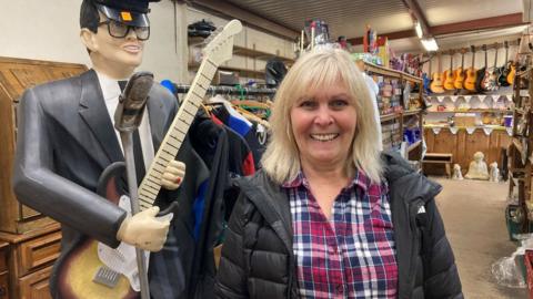 Teresa Woods, Co-owner of Wot Not standing beside a life size prop of a man playing a guitar