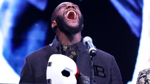 Deontay Wilder shouts with a mask in his hand