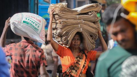 A woman carries a stack of paper bags at a wholesale market in the commercial hub of Colombo, Sri Lanka.
