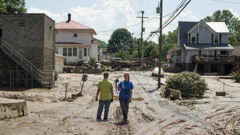 People stand in mud covered street after flooding of Elk River on June 25, 2016 in Clendenin, West Virginia