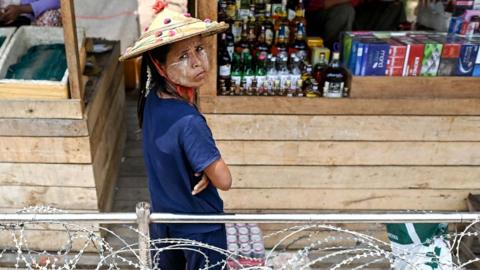 A Myanmar vendor (C) selling alcohol, cigarettes and aphrodisiac looks on while waiting for customers inside a "no-man's land" between Thailand and Myanmar, as seen from behind a barb-wire fence in Thailand's Mae Sot district on April 12, 2024