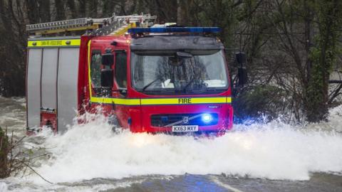 A Cumbria fire engine drives through water on a flooded road