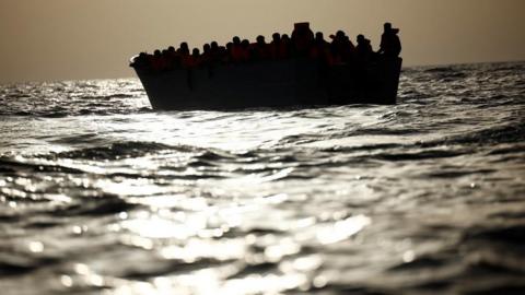Migrants (seen in silhouette) wait in a boat during a search and rescue operation in the Mediterranean.