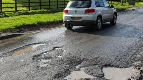 A car driving by a series of potholes in Slough, 2023