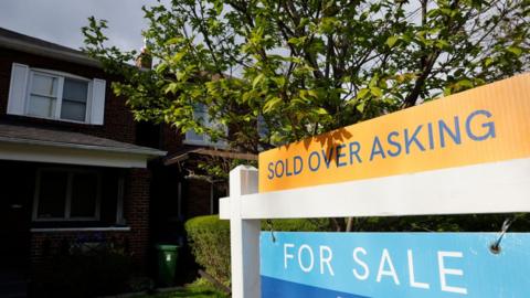 A 'SOLD OVER ASKING' sign is displayed outside a property near the intersection of Manor Rd. E. and Forman Ave. in Toronto.