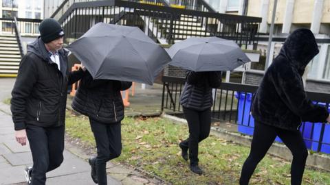 Elliot Benham (second left under umbrella) and Sophie Harvey (second right under umbrella) leave Cheltenham Magistrates' Court