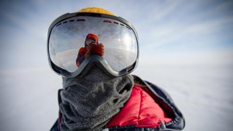 Person wearing a large pair of goggles - in icy Antarctic landscape... also a warm coat and scarf