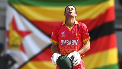 Sean Williams, batting in an ODI for Zimbabwe, leans his head back with a Zim flag hanging in the background